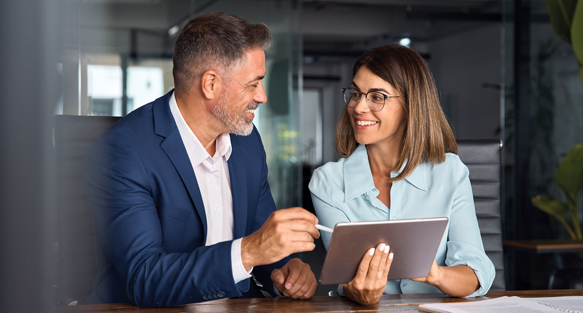 a man and woman smiling and talking while holding a tablet