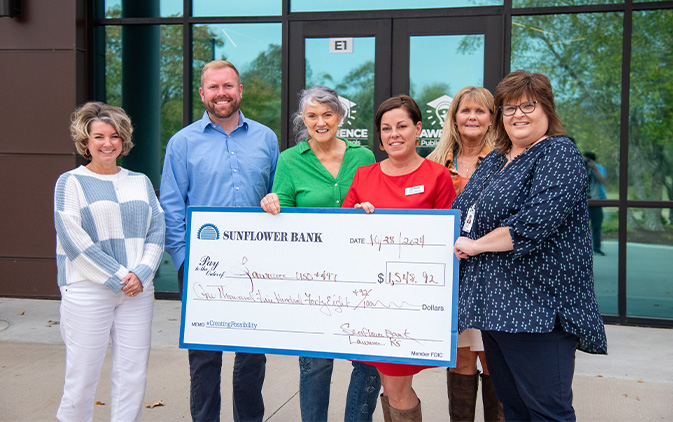six people holding a large Sunflower Bank check in front of a glass building