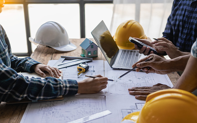 individuals sitting at table with construction hats and building plans