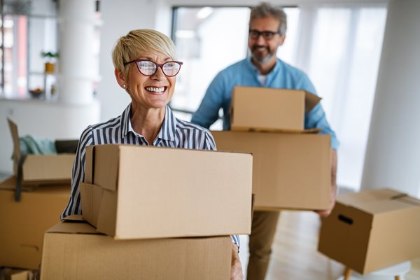 A woman and man holding boxes moving into house