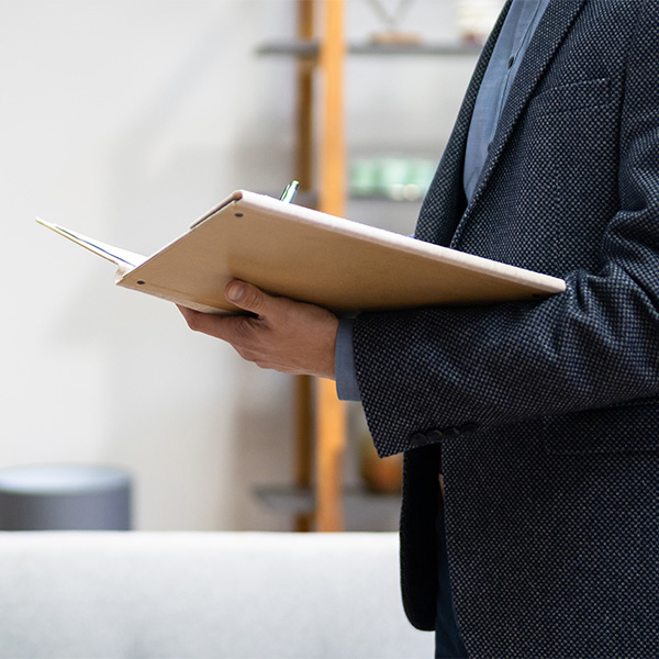 person in suit in a house writing in brown notepad