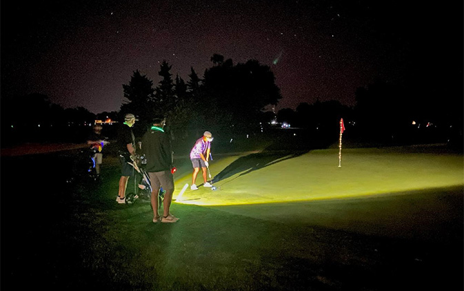 individuals putting on golf green at night with glow sticks