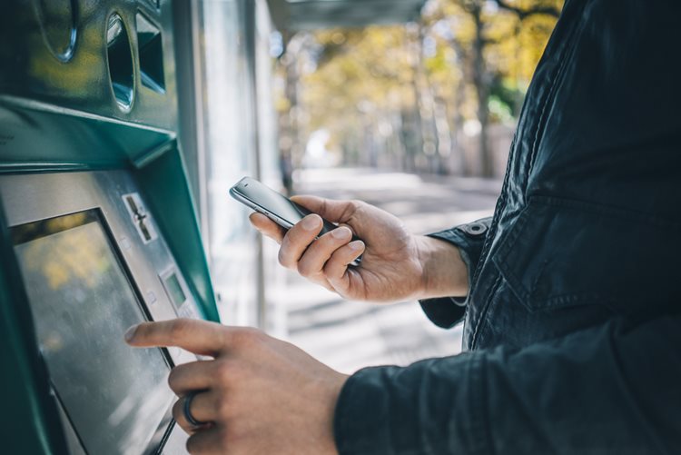 Person holding phone and using ATM