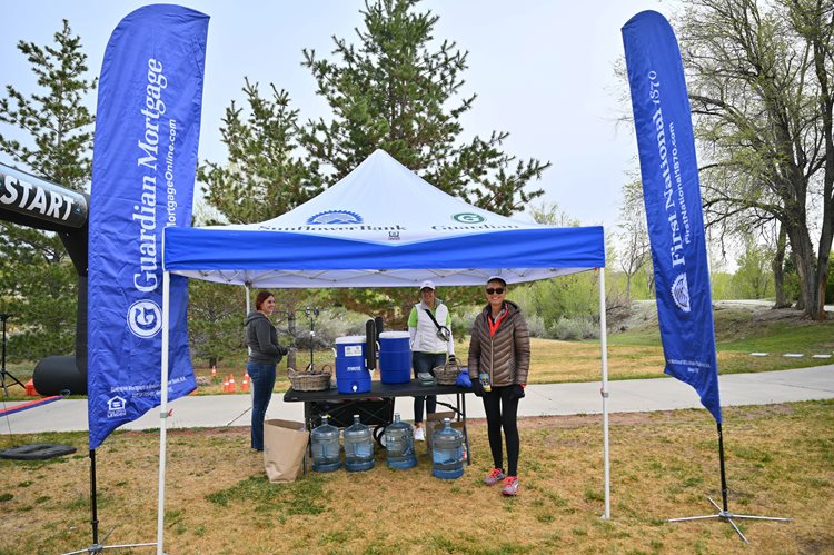 three volunteers standing under a blue tent with flags