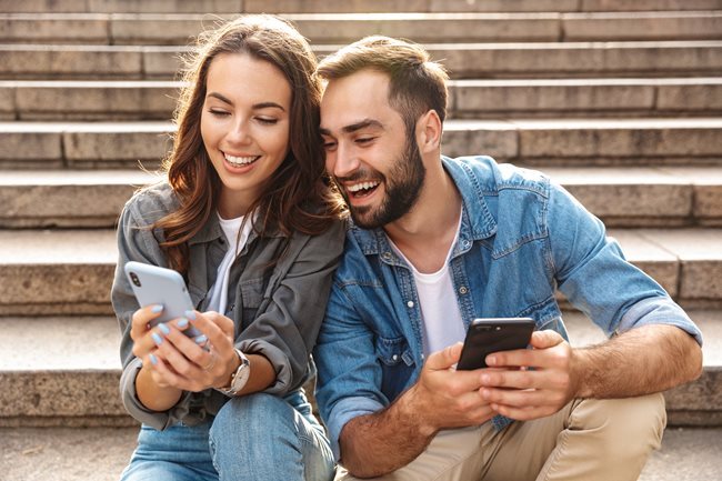 woman and man smiling looking at their phones