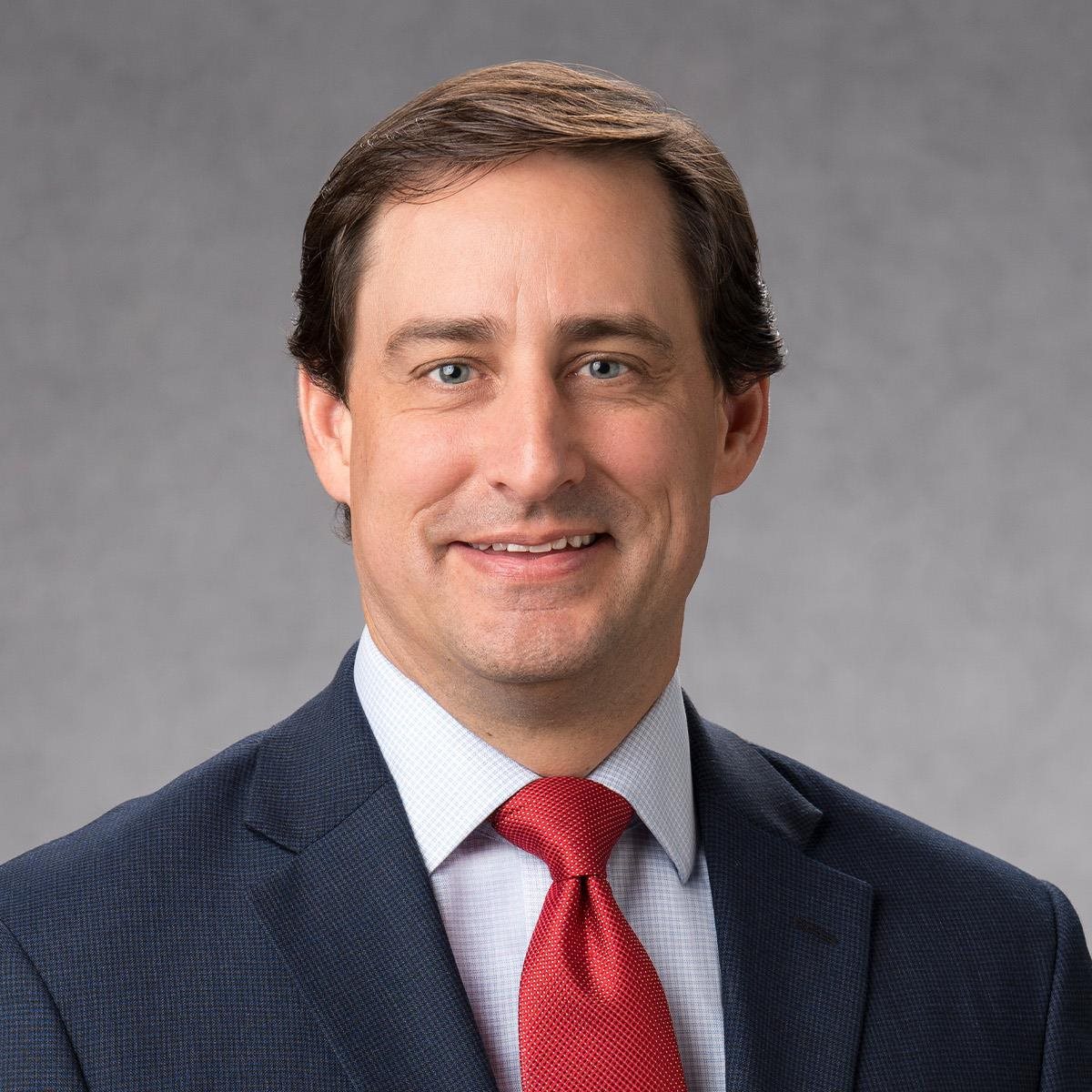 Headshot of Dan Leonard in black suit with red tie