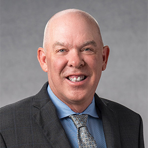 Headshot of Scott Downey in black suit and blue shirt with tie
