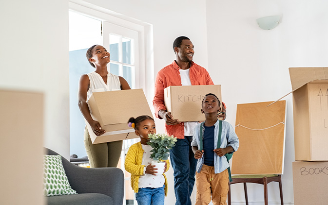 family of four walking into new house with moving boxes