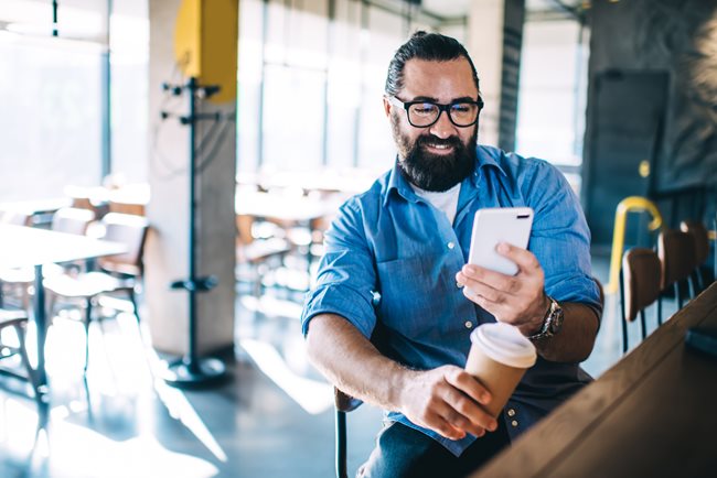 Man holding a coffee looking at phone