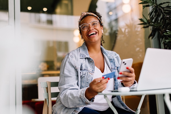 women in coffee shop with phone and credit card in hand smiling