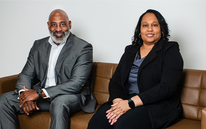 two employees in suits sitting on brown leather couch